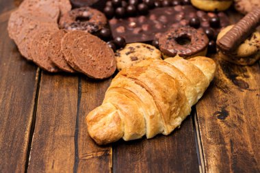 Çikolata dolgulu taze kruvasan ve kırsal arka planda çeşitli çikolatalar ve kurabiyeler.