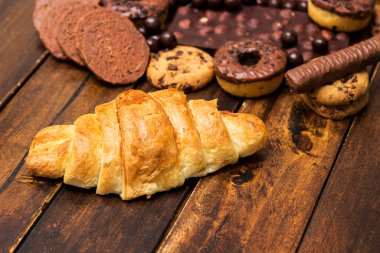 Çikolata dolgulu taze kruvasan ve kırsal arka planda çeşitli çikolatalar ve kurabiyeler.