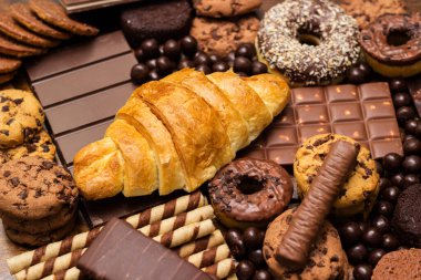 Çikolata dolgulu taze kruvasan ve kırsal arka planda çeşitli çikolatalar ve kurabiyeler.