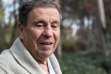 Sonbahar parkında gülümseyen yaşlı bir adamın portresi.