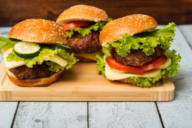 Etli, peynirli ve marullu hamburgerler kesme tahtasında servis edilir.