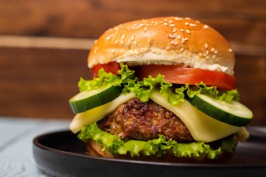 Köfte ve peynirli hamburger, siyah tabakta servis edilir.