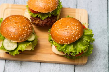 Etli, peynirli ve marullu hamburgerler kesme tahtasında servis edilir.