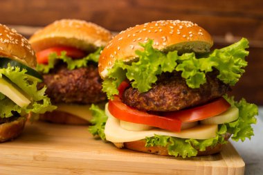 Etli, peynirli ve marullu hamburgerler kesme tahtasında servis edilir.