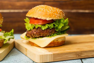 Etli, peynirli ve marullu hamburgerler kesme tahtasında servis edilir.