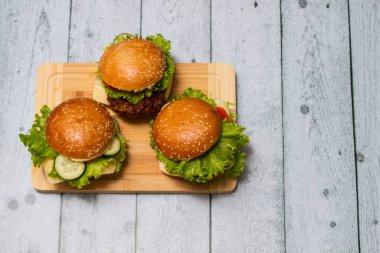 Etli, peynirli ve marullu hamburgerler kesme tahtasında servis edilir.