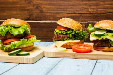 Etli, peynirli ve marullu hamburgerler kesme tahtasında servis edilir.