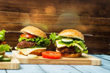 Etli, peynirli ve marullu hamburgerler kesme tahtasında servis edilir.