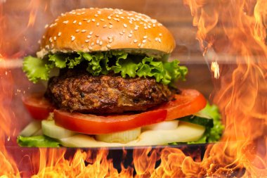 Buhar dumanlı leziz sığır etli hamburger ve arka planda ateş alevleri.