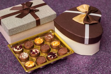 Lezzetli çikolata şekerleri ve kalp şeklinde hediyelerle dolu bir kutu, mor masanın üzerinde.