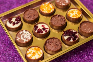 Mor masanın üzerinde lezzetli çikolata şekerleri olan altın kutu.