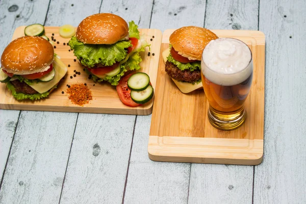 Tasty burgers and beer, beef burgers with lettuce and cheese on wood table