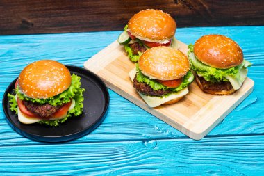 Tahta bir masada et, peynir, marul, domates ve ev yapımı hamburgerler.