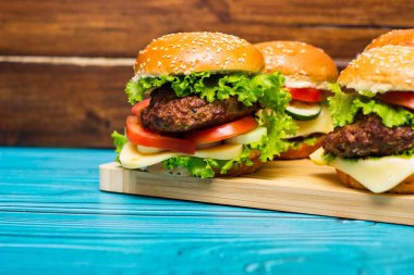 Tahta bir masada et, peynir, marul, domates ve ev yapımı hamburgerler.