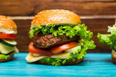 Tahta bir masada et, peynir, marul, domates ve ev yapımı hamburgerler.