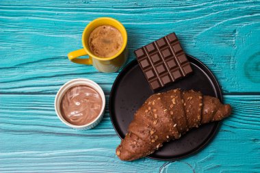 Coffee break with chocolate pastry. Cup of cappuccino coffee with croissant. Coffee and croissant on table