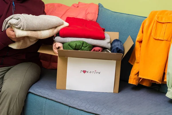 Woman holding clothes with Donate Box In her room. Gathering items to be donated to charity