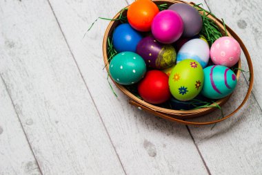 Tahta masanın üzerinde renkli paskalya yumurtaları olan sepet.