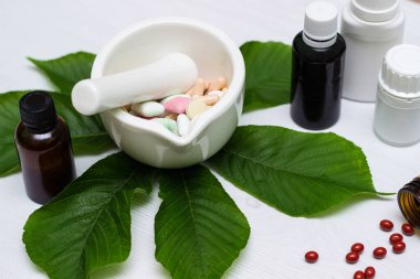 Variation of vitamins and pills on a green leaf on a white background