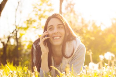 Woman enjoying the sun outdoors in sunset, talking on the smartphone