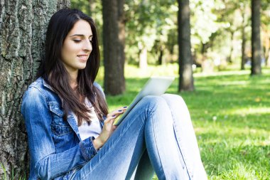 Parkta dijital tablet kullanan güzel bir kadın.