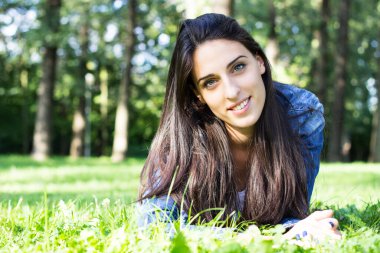 Beautiful young female lying on grass, looking at the camera. In the park.