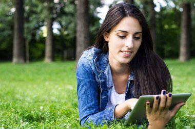 Parkta dijital tablet kullanan güzel bir kadın.