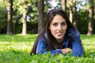 Beautiful young female lying on grass, looking at the camera. In the park.