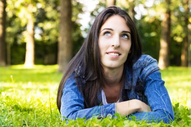 Beautiful young female lying on grass, looking at the camera. In the park.