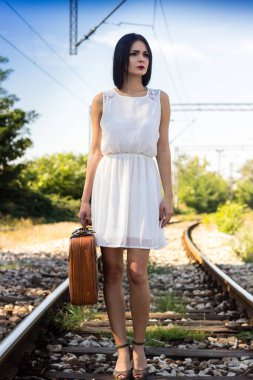 Woman walking on railroad tracks with suitcase