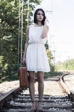 Woman walking on railroad tracks with suitcase