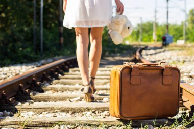 Woman walking on railway with suitcase and teddy bear
