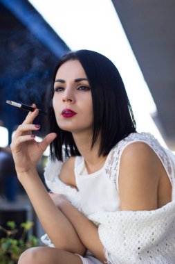 Young woman sitting on a railway station and smokes a cigar