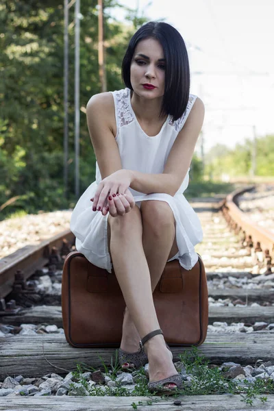 Beautiful woman sitting on a suitcase and waiting for the train