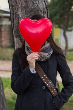 Gülen kız elinde balondan bir kalp tutuyor.