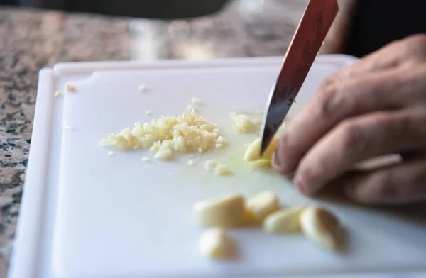 Close up of the hands of a chef cutting garlic on a kitchen board