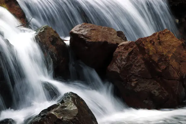 stock image Water flows down a small waterfall cascading down a rocky cliff.