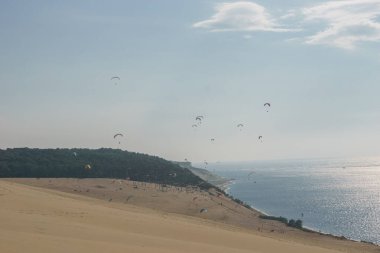 Güneşli bir günde, Arcachon, Nouvelle-Aquitaine, Fransa 'da, Pilat tepesinde rüzgarlı havada uçan çok sayıda paraşütçü var.