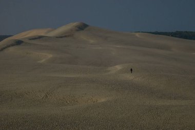 Büyük kum formasyonunda yürüyen tek bir adam silueti Dune du Pilat gece ay ışığıyla aydınlatılır, Arcachon, Yeni Aquitaine, Fransa