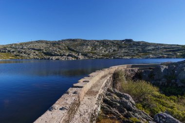 Güneşli bir sonbahar gününde, az bitki örtüsü ve göl barajı olan kayalık bir arazi. Torre, Serra da Estrela, Portekiz.
