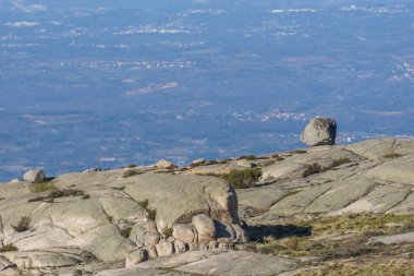 Tek mermili yıkanmış taş, bir dağ manzarasının kayalık yüzeyinde, vadideki uzak puslu manzaralı, Serra da Estrela, Portekiz