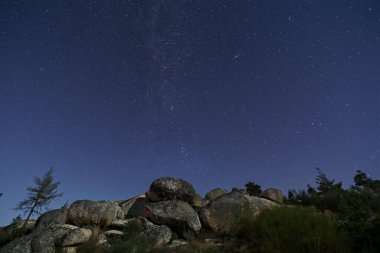 Kış Samanyolu ve Andromeda Galaksisi ay ışığıyla aydınlatılan kayalık ve saf bir manzara üzerinde, Vale do Rossim, Serra da Estrela, Portekiz