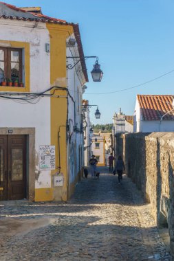 Evora 'nın dar asfalt sokak manzarası, sıcacık beyaz ve sarı evler, Evora, Alentejo, Portekiz