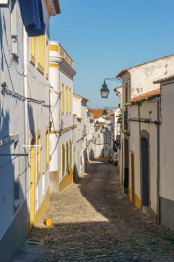 Evora 'nın dar asfalt sokak manzarası, sıcacık beyaz ve sarı evler, Evora, Alentejo, Portekiz