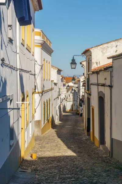 Evora 'nın dar asfalt sokak manzarası, sıcacık beyaz ve sarı evler, Evora, Alentejo, Portekiz