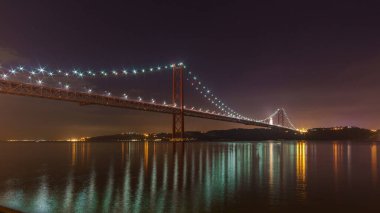 Aydınlatılmış kırmızı köprü 25 de Abril Köprüsü Tagus Nehri 'ni gece vakti Cristo Rei heykeliyle geçiyor, Lizbon, Portekiz