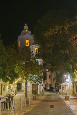 Geceleri, Portekiz, Algarve Lagos 'taki Katolik Kilisesi' nin önündeki ağaçlarla şehir manzarası.