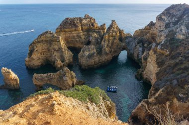 Ponta da Piedade yakınlarındaki Atlantik kıyı şeridinin ünlü kayalık oluşumu. Berrak mavi su koyunda teknesi olan Lagos, Algarve, Portekiz..