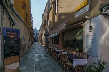 Güneşli bir sabah Venedik, Venedik, Veneto, İtalya 'da tipik ön cepheleri ve pizza masaları olan eski bir sokak.