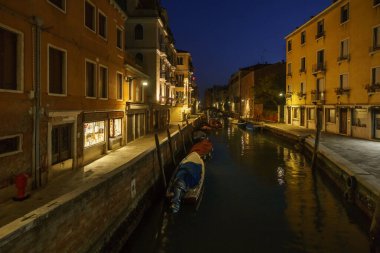 Bir kış gecesi Venedik, Venedik, Veneto, İtalya 'da mavi saatte tekneli renkli bina cepheleriyle çevrili tipik bir kanal manzarası.